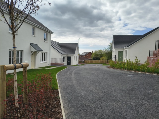 A street view of newly built houses and bungalows with young trees and landscaping on the Beacon Cymru development at Llannon