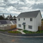 A newly built white detached house with a grey-tiled roof on the Beacon Cymru development at Llannon, with a solar-panelled bungalow alongside