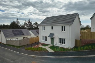 A newly built white detached house with a grey-tiled roof on the Beacon Cymru development at Llannon, with a solar-panelled bungalow alongside