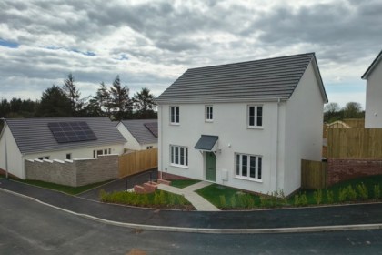 A newly built white detached house with a grey-tiled roof on the Beacon Cymru development at Llannon, with a solar-panelled bungalow alongside