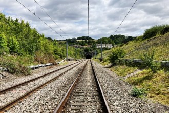 Railway tracks leading towards the mouth of Chipping Sodbury tunnel, with overhead lines and green embankments either side.