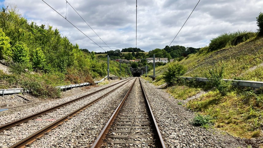 Railway tracks leading towards the mouth of Chipping Sodbury tunnel, with overhead lines and green embankments either side.
