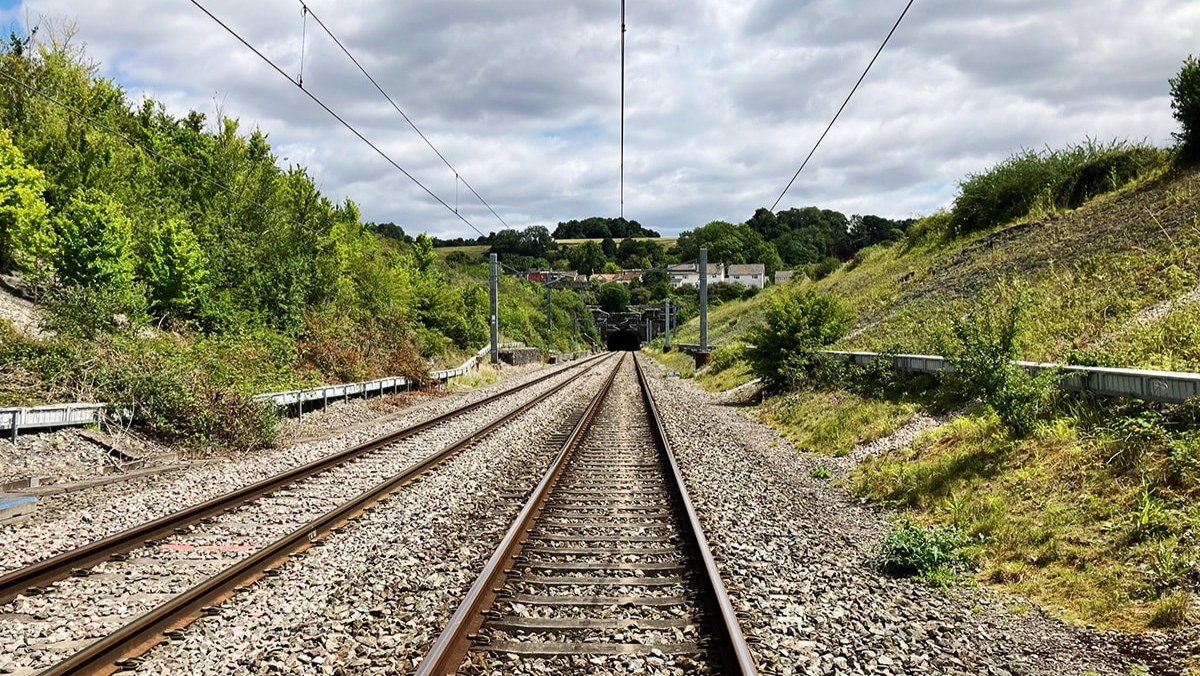 Railway tracks leading towards the mouth of Chipping Sodbury tunnel, with overhead lines and green embankments either side.