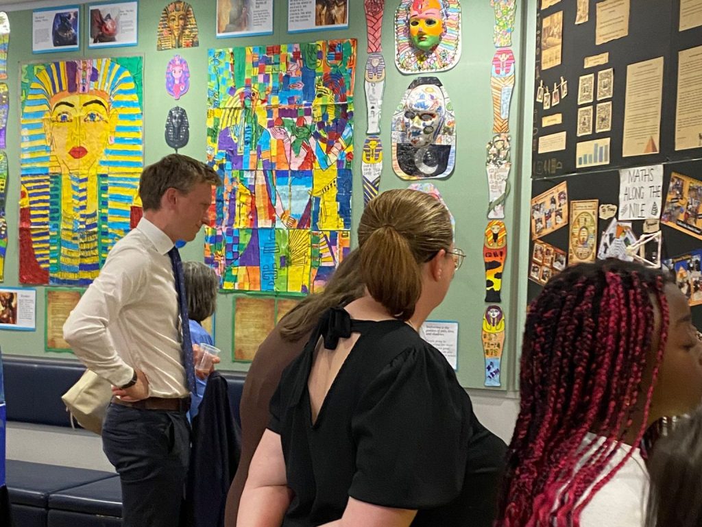 Torsten Bell and other guests look at a wall of brightly coloured pupil artwork showing Tutankhamun masks and Egyptian figures at the Egypt Centre.