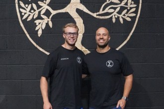 Elysium Training Club co-founders Peter Crudge and Andrew Finnegan stand smiling in front of a tree-of-life mural at their new Swansea gym.