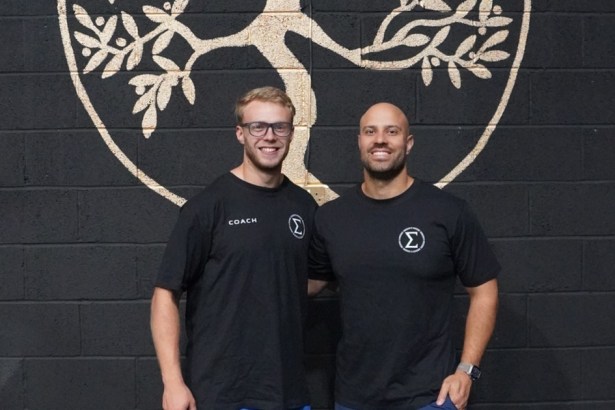 Elysium Training Club co-founders Peter Crudge and Andrew Finnegan stand smiling in front of a tree-of-life mural at their new Swansea gym.