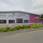 A visualisation of a large industrial building rebranded in Gower College Swansea's grey and magenta livery, with college signage and a workshop entrance