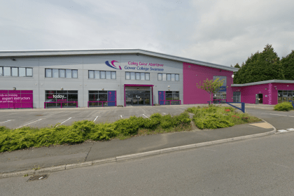 A visualisation of a large industrial building rebranded in Gower College Swansea's grey and magenta livery, with college signage and a workshop entrance