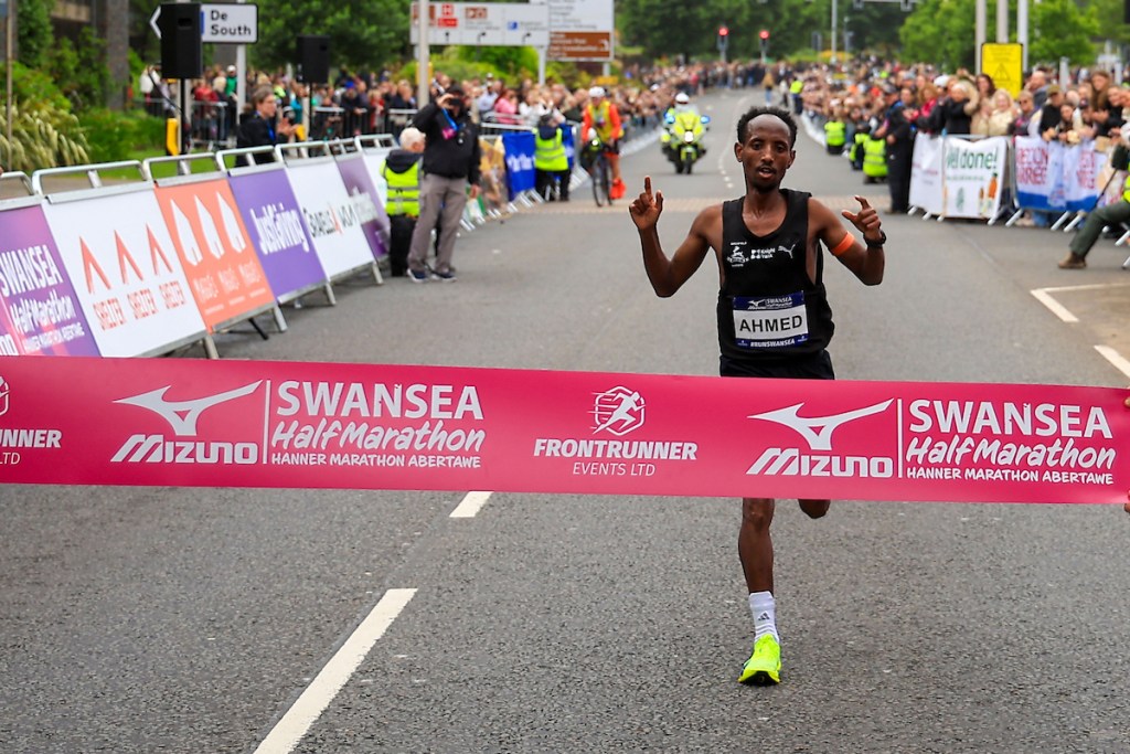 Men's winner Omar Ahmed crossing the finish line through the race tape.