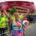 Women's winner Rose Harvey holding the finish tape above her head, wearing her medal.