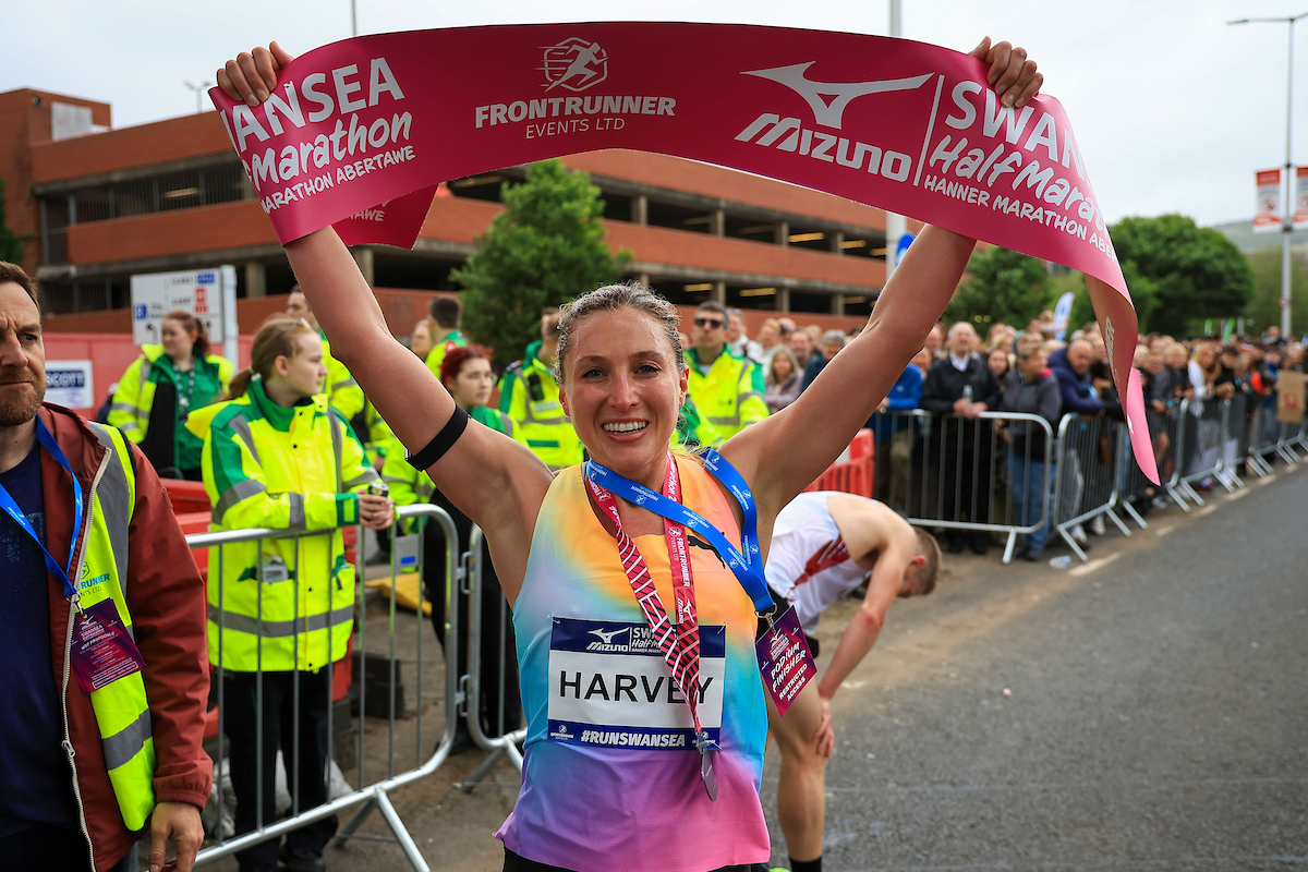 Women's winner Rose Harvey holding the finish tape above her head, wearing her medal.