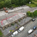 Aerial view of the part-demolished former Godre'rgraig Primary School, with an excavator working on cleared ground and rubble beside the remaining arched stone wall along Graig Road.