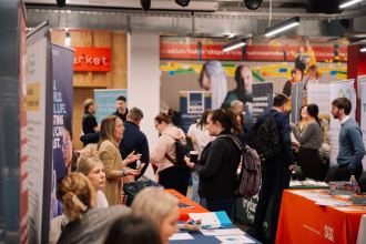 Graduates and employers talking at exhibitor stands during a GradCon careers fair, with banners and information stalls