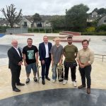 Six people standing on the concrete bowl of the new Victoria Park skatepark, two holding skateboards, with houses and trees behind.