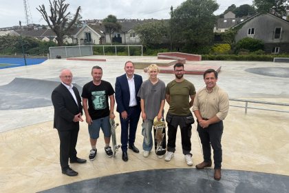 Six people standing on the concrete bowl of the new Victoria Park skatepark, two holding skateboards, with houses and trees behind.