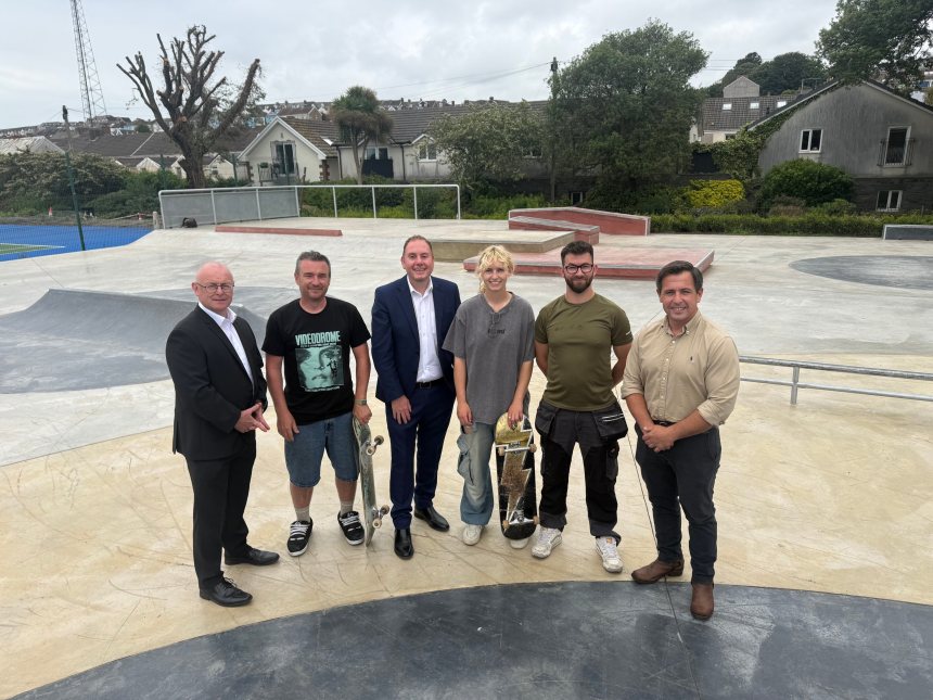 Six people standing on the concrete bowl of the new Victoria Park skatepark, two holding skateboards, with houses and trees behind.