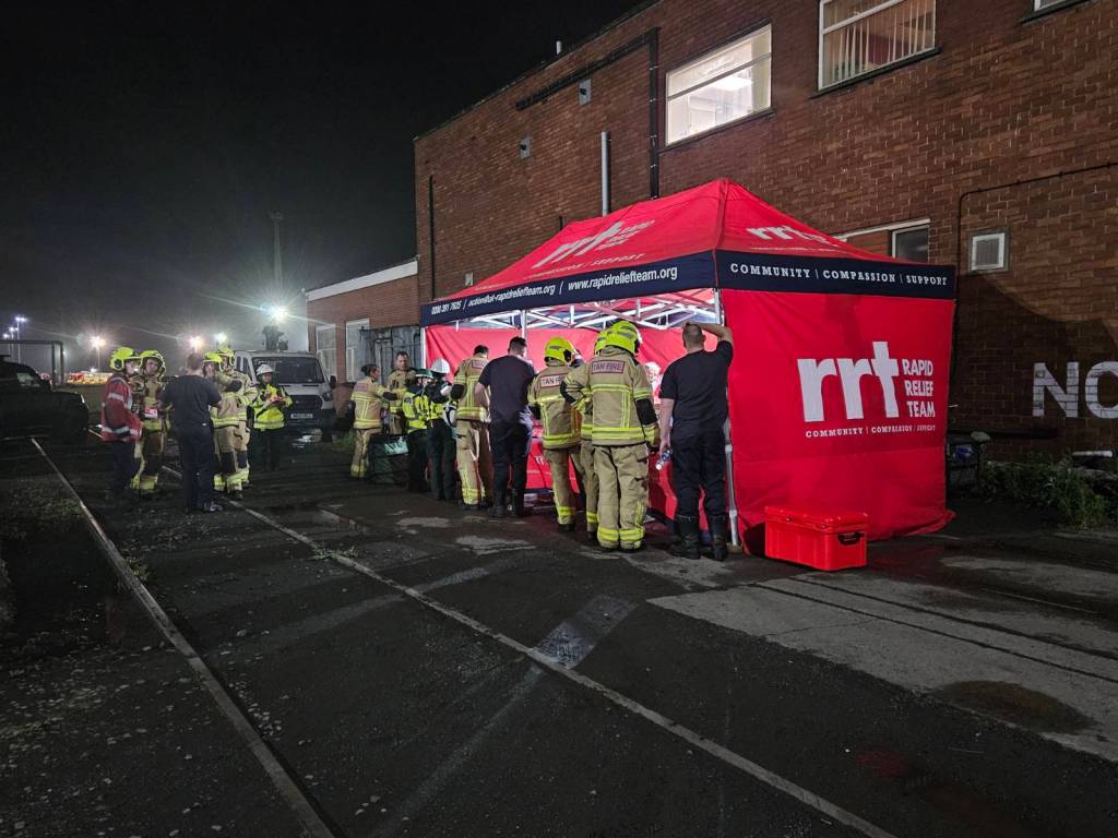 Firefighters and ambulance crews gather at a red Rapid Relief Team catering tent at night