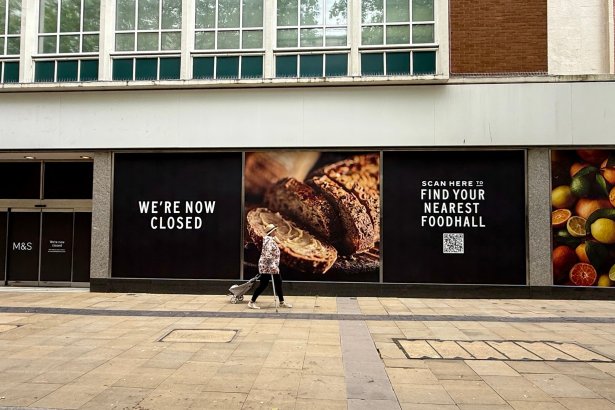 Boarded and blacked-out M&S store windows on Oxford Street, Swansea, with a lone shopper passing by