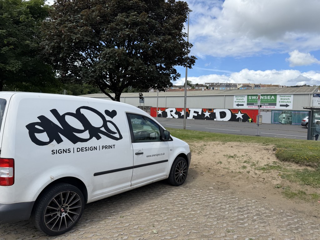 White Oner Signs van in the foreground with the giant RFD graffiti tribute visible on the St Helen's stadium wall behind