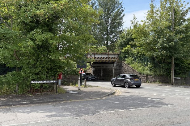 The Fairwood Terrace street sign at its junction with Victoria Road, Gowerton, with a low stone railway bridge crossing the road ahead and traffic passing through — the site of a proposed traffic signal-controlled junction.