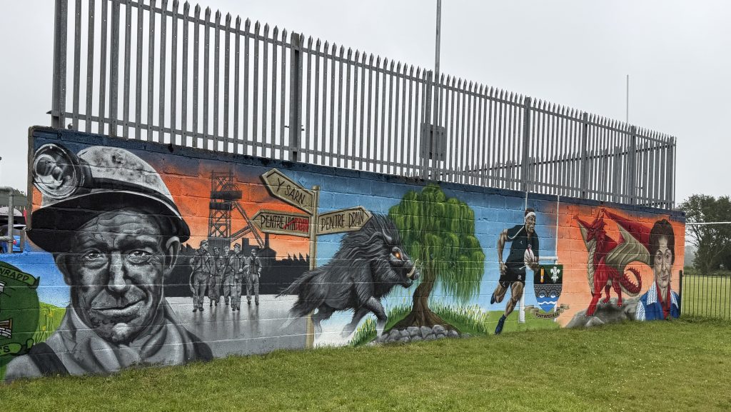 A section of mural showing a miner, a wild boar, a willow tree, a rugby player and a Welsh dragon.