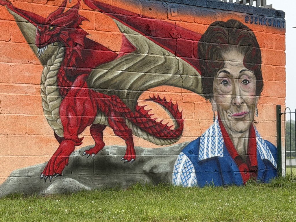 Mural detail of a red Welsh dragon beside a painted portrait of Dot Cotton.