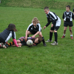 Young children playing junior rugby on a grass pitch, contesting the ball.