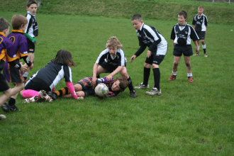 Young children playing junior rugby on a grass pitch, contesting the ball.