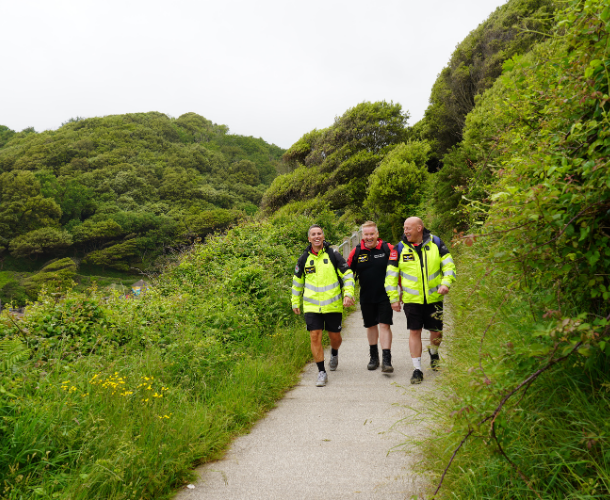 Three air ambulance medics in hi-vis jackets walking along a green coastal path.