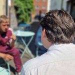 An outreach worker sits talking with a man at an outdoor table at a homelessness drop-in centre.