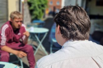 An outreach worker sits talking with a man at an outdoor table at a homelessness drop-in centre.