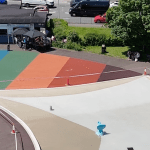 Aerial view of the drained Blackpill Lido, fenced off with hazard tape and traffic cones, the rainbow-coloured surround empty apart from a few people by the kiosk.