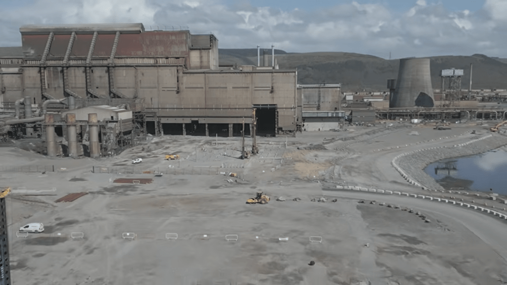 A vast cleared industrial yard with a single roller and demolished plant buildings behind.