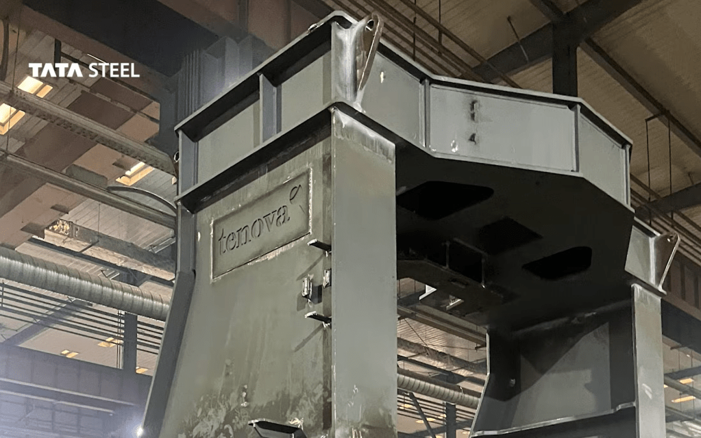 A large grey steel furnace component bearing the Tenova logo, inside a fabrication hall