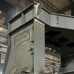 A large grey steel furnace component bearing the Tenova logo, inside a fabrication hall