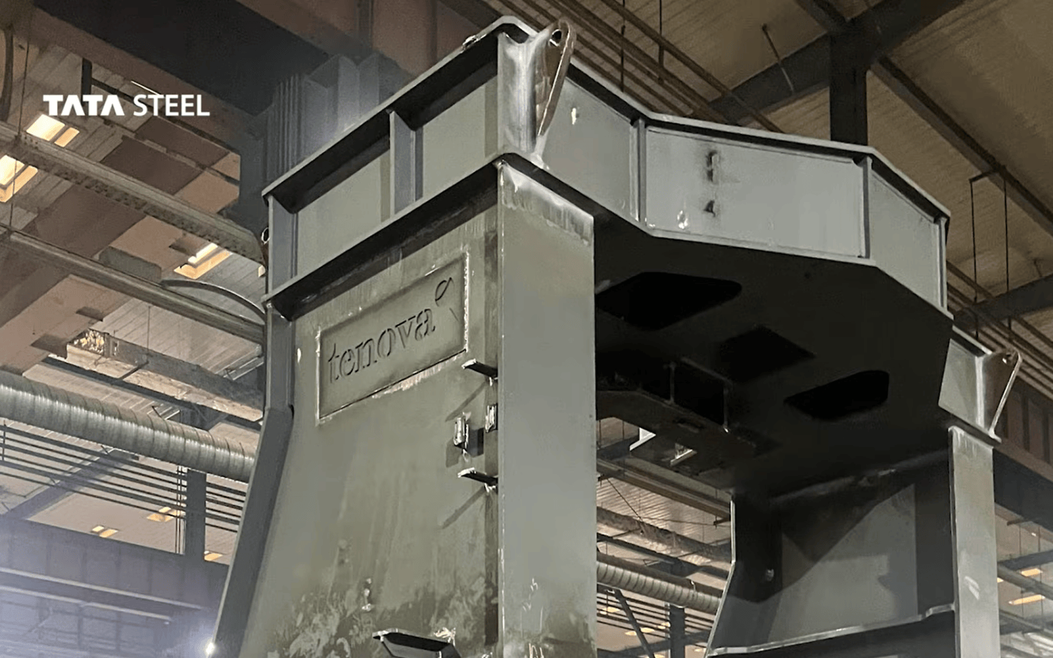 A large grey steel furnace component bearing the Tenova logo, inside a fabrication hall