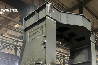 A large grey steel furnace component bearing the Tenova logo, inside a fabrication hall