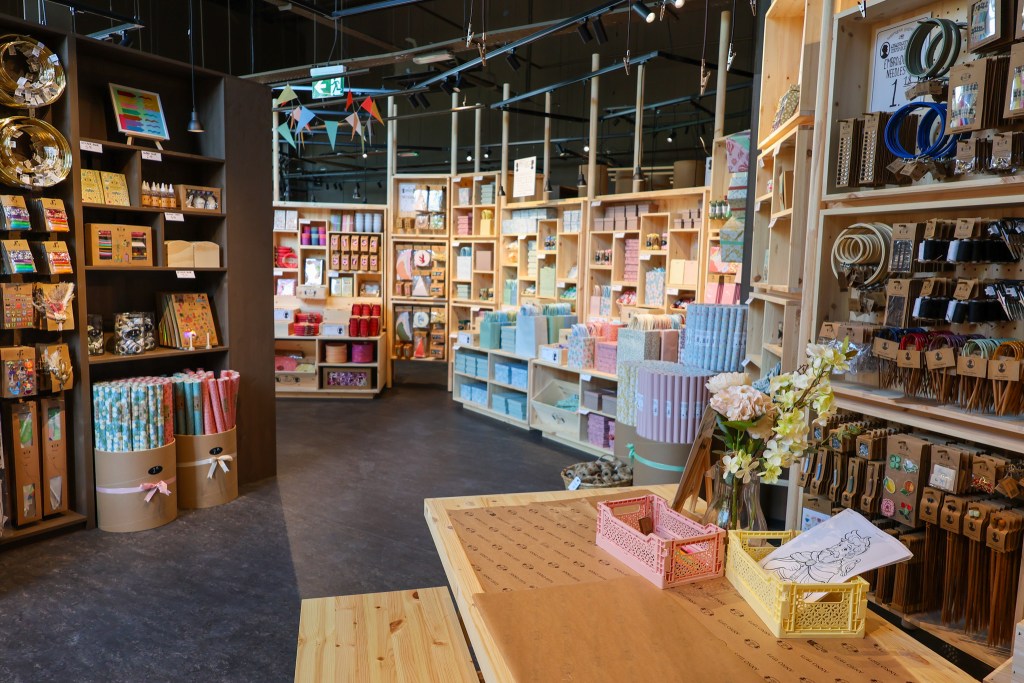 The craft and stationery section of the store, with wrapping paper, ribbons and embroidery supplies on wooden shelves.