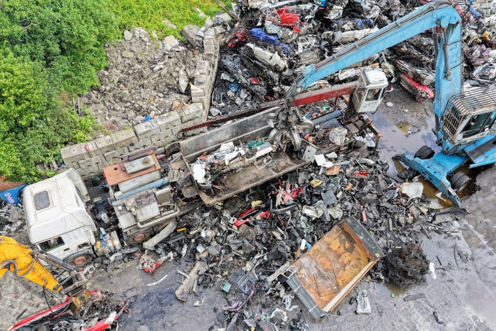 Aerial view of flattened white van wreckage among piles of crushed cars at a scrapyard