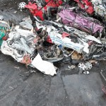 Aerial view of a scrapyard crane lifting crushed vehicle remains from a pile of scrap metal