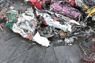 Aerial view of a scrapyard crane lifting crushed vehicle remains from a pile of scrap metal