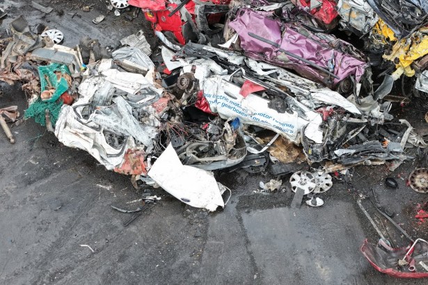 Aerial view of a scrapyard crane lifting crushed vehicle remains from a pile of scrap metal