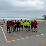 A group of walkers, including air ambulance crew in hi-vis jackets, on a beachside promenade with the sea behind.