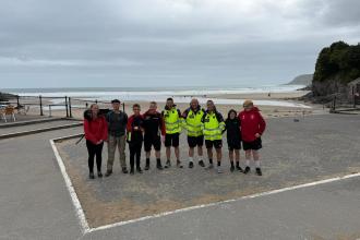 A group of walkers, including air ambulance crew in hi-vis jackets, on a beachside promenade with the sea behind.