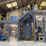 Large grey industrial casting furnace and steel gantry inside the Wall Colmonoy plant in Pontardawe.