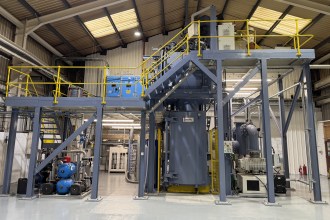 Large grey industrial casting furnace and steel gantry inside the Wall Colmonoy plant in Pontardawe.