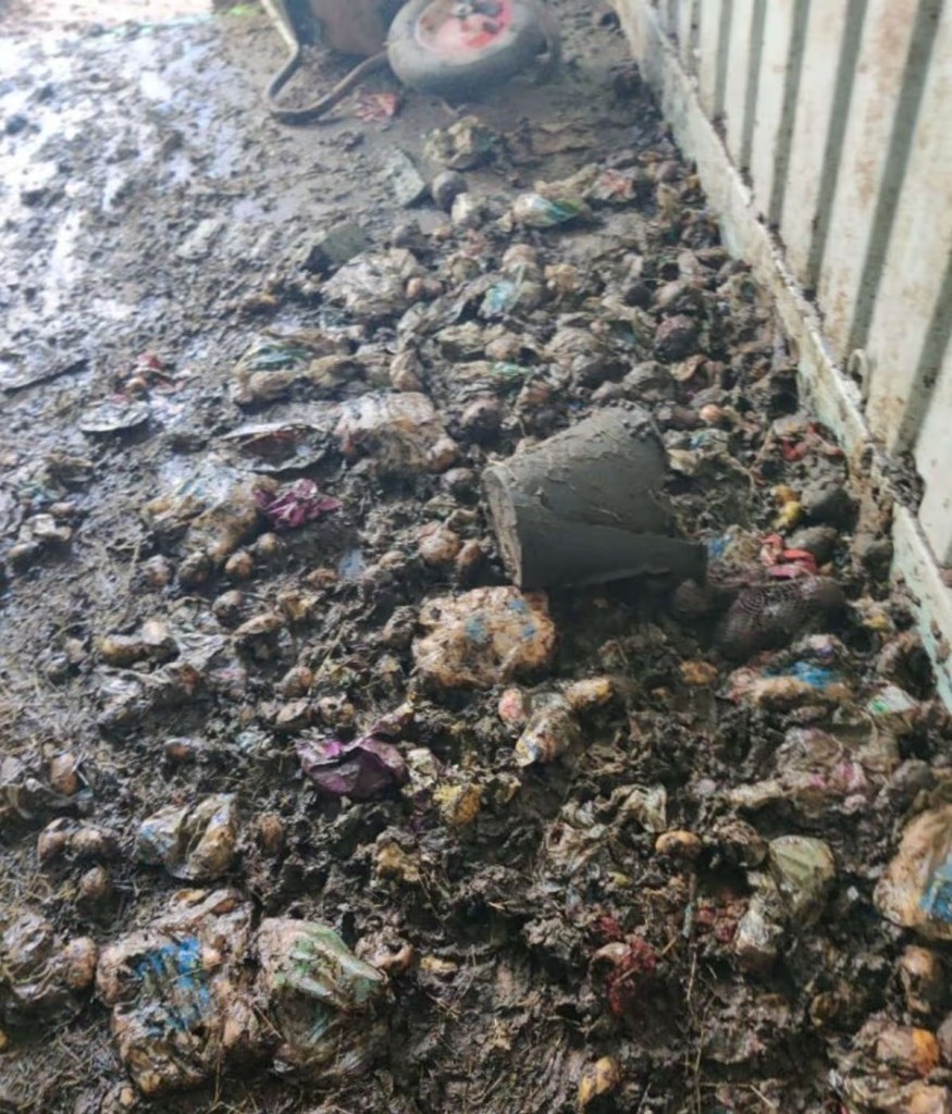 The floor of a metal-sided container covered in decomposing food waste, packaging and mud.
