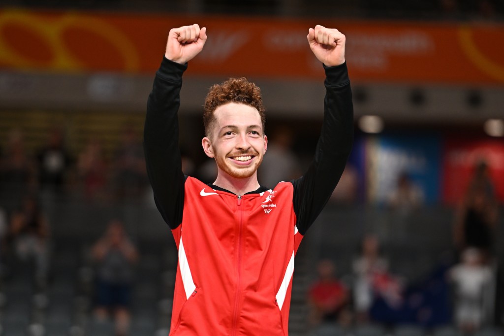 Cyclist Will Roberts raising both fists in celebration in his Wales tracksuit.