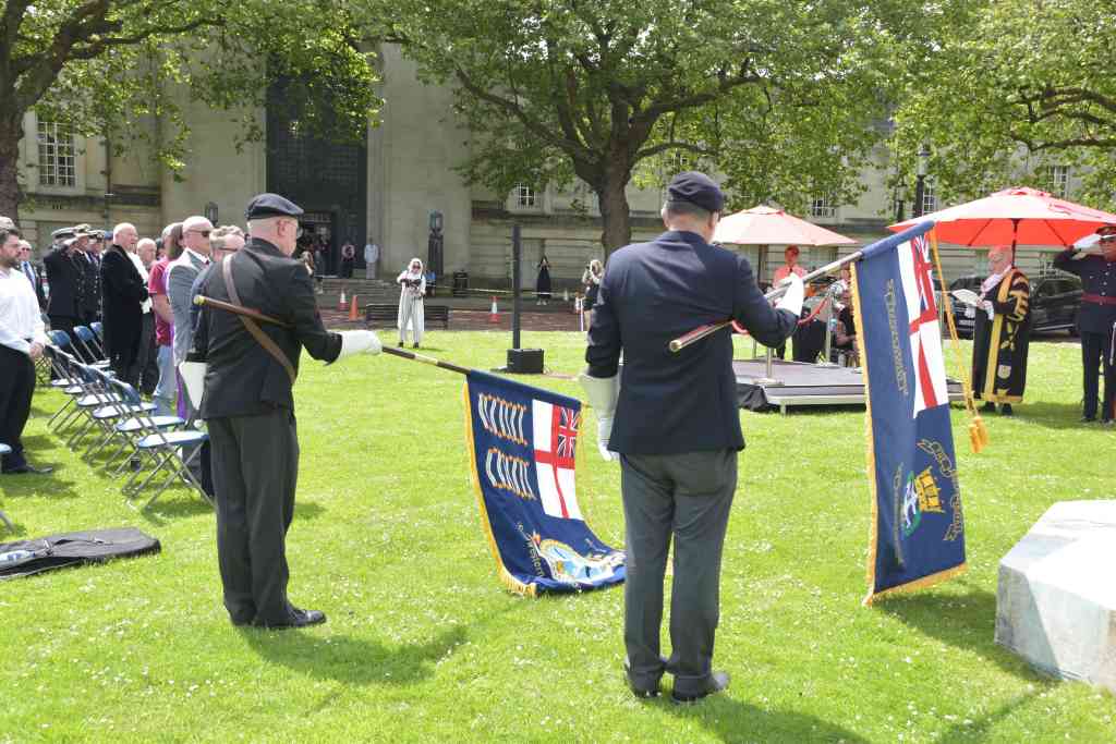 Two standard-bearers in berets lower ceremonial flags on the Guildhall lawn, with the Lord Mayor and a saluting officer in the background.