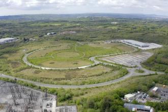 Aerial view of Parc Felindre business park near Swansea, with looping internal roads, empty green plots, an electricity substation and a single large distribution centre.